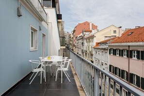 Ein Balkon mit Tisch und Stühlen, mit Blick auf eine Reihung von Gebäuden mit roten Ziegeldächern.