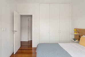 A bedroom with a bed, a wardrobe, a nightstand, and a door leading to another room. - GuestReady - Modern essence near Estrela Garden (Lisbon)