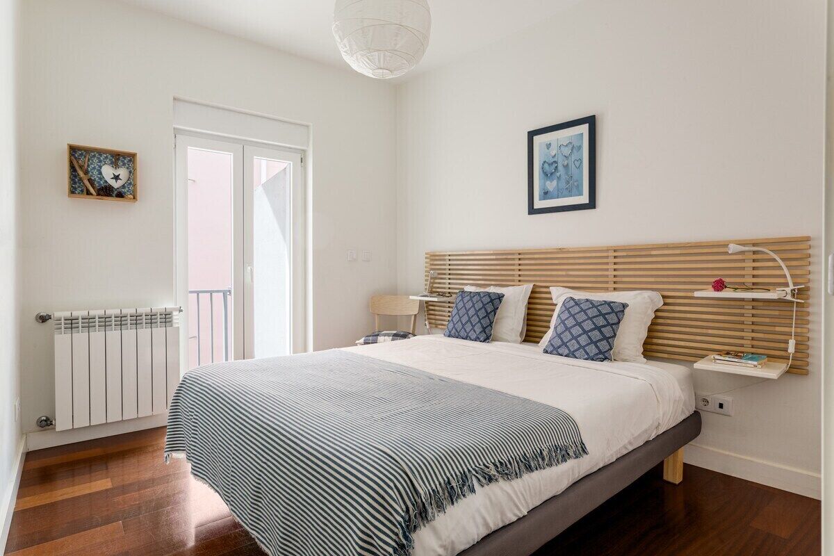 A bedroom with a bed, bedside table, and a window with blinds.