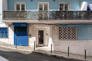 A two-story building with a blue facade, a metal balcony railing, and a closed blue door. - GuestReady - Modern essence near Estrela Garden (Lisbon)