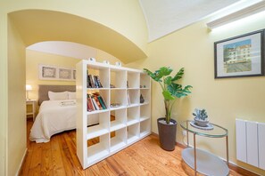 A hotel room with a bed, a white bookshelf, a potted plant, a framed picture, and a small table. - GuestReady - Cosy studio near Santa Justa Lift (Lisbon)