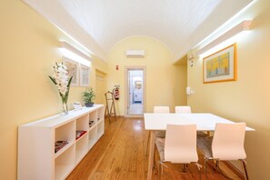 A hotel room with a wooden floor, a white reception desk, a white dining table with chairs, and a painting on the wall. - GuestReady - Cosy studio near Santa Justa Lift (Lisbon)