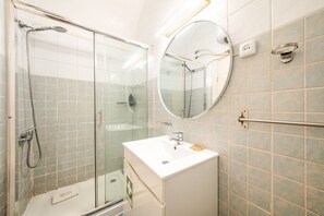 Ett badrum med en dusch som är avskärmad med glasväggar, ett vitt handfat och en rund spegel.