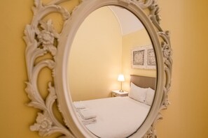 A room with a bed, a nightstand, a lamp, and a mirror with ornate frame. - GuestReady - Cosy studio near Santa Justa Lift (Lisbon)