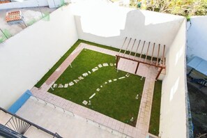 Une terrasse sur le toit avec une petite pelouse, un espace salon avec une table et des chaises, et une rambarde en métal.