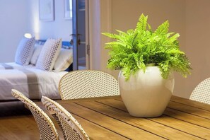 A room with a wooden dining table, a white vase with green foliage, wicker chairs, and a bed with white bedding in the background. - GuestReady - Stunning duplex near Santa Justa Lift (Lisbon)