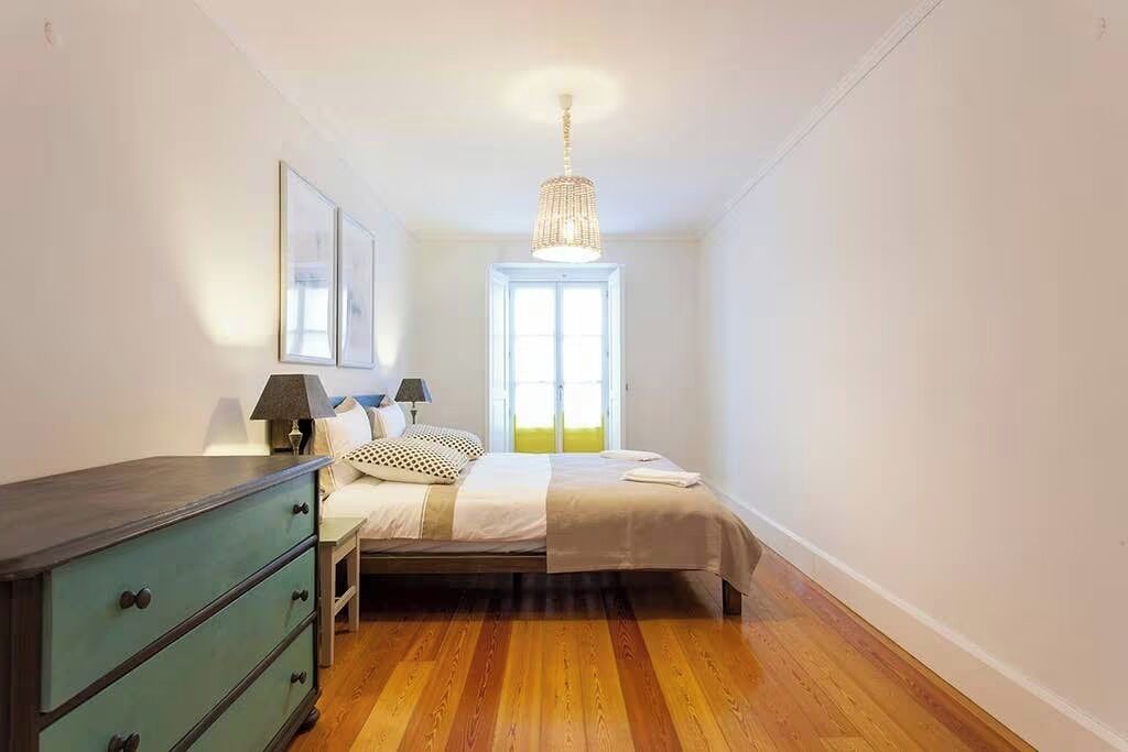 Un dormitorio con cama, cómoda, ventana y candelabro.