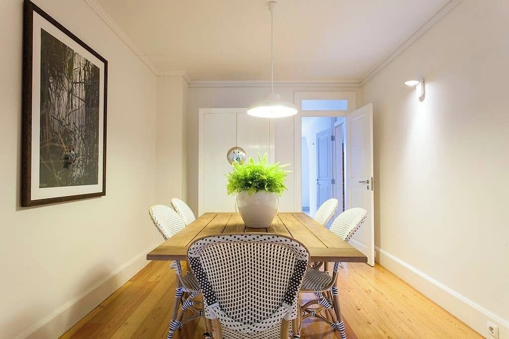 A dining area with a wooden table, white chairs, a potted plant, and a framed picture on the wall.