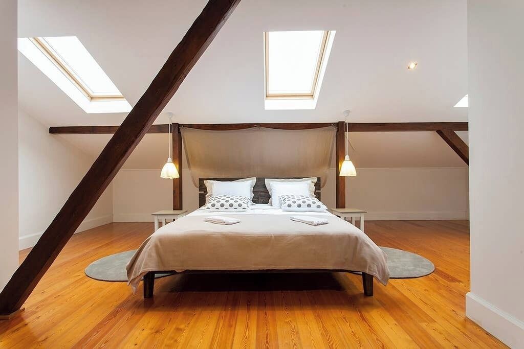 A bedroom with a sloped ceiling, skylights, a bed with pillows, bedside tables, and a circular rug.