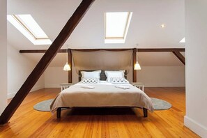 A bedroom with a sloped ceiling, skylights, a bed with pillows, bedside tables, and a circular rug. - GuestReady - Stunning duplex near Santa Justa Lift (Lisbon)