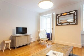 Une pièce comprenant un meuble sur lequel est posée une télévision, un fauteuil en osier, un miroir et un tapis à motifs.