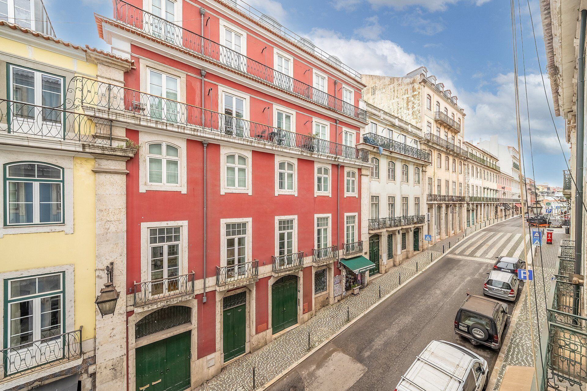 A street view with multi-story buildings, a cobblestone street, and parked cars.