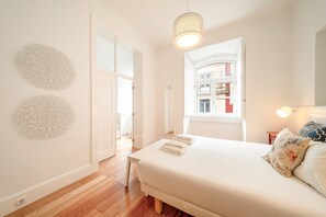 A bedroom with a bed, a bedside lamp, a window with a view of buildings, and decorative wall art. - GuestReady - Chic apt near Lisbon Cathedral (Lisbon)