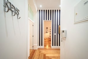 A hallway with striped wallpaper, a wooden floor, and a door leading to a room with a desk and chair. - GuestReady - Chic apt near Lisbon Cathedral (Lisbon)