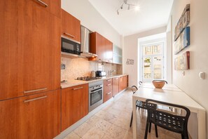 A compact kitchen with wooden cabinets, a built-in oven, and a dining area with a table and chairs. - GuestReady - Chic apt near Lisbon Cathedral (Lisbon)