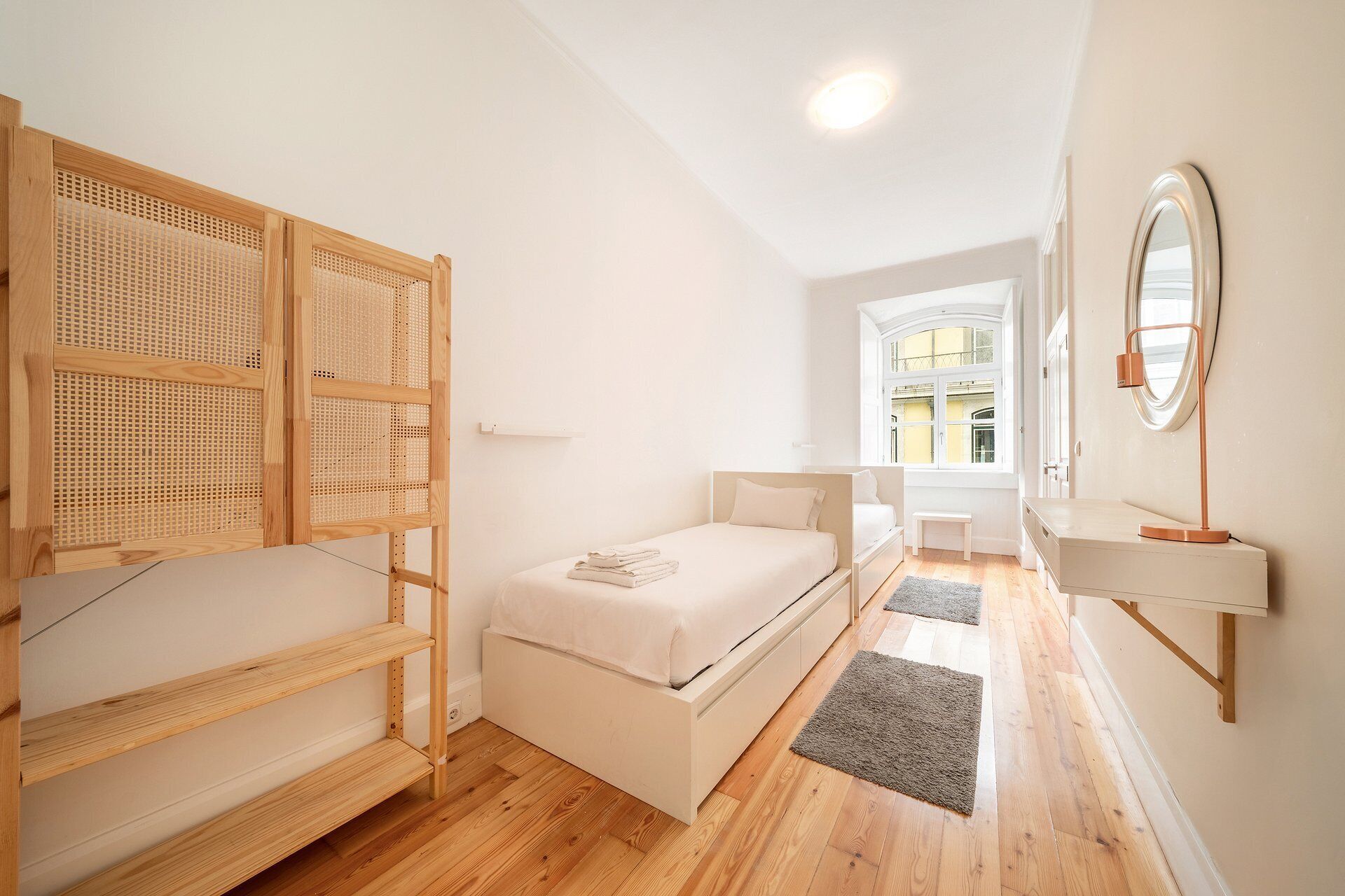 A bedroom with a bed, a bedside table, a mirror, and a window.
