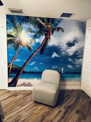 Een kamer met een muurschildering van een strand, een witte fauteuil en houten vloeren.