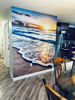 A dining area with a wall mural of a beach at sunset, a wooden dining table, and a chair. - West Melboburne Oasis, minutes to the beach! (Melbourne)