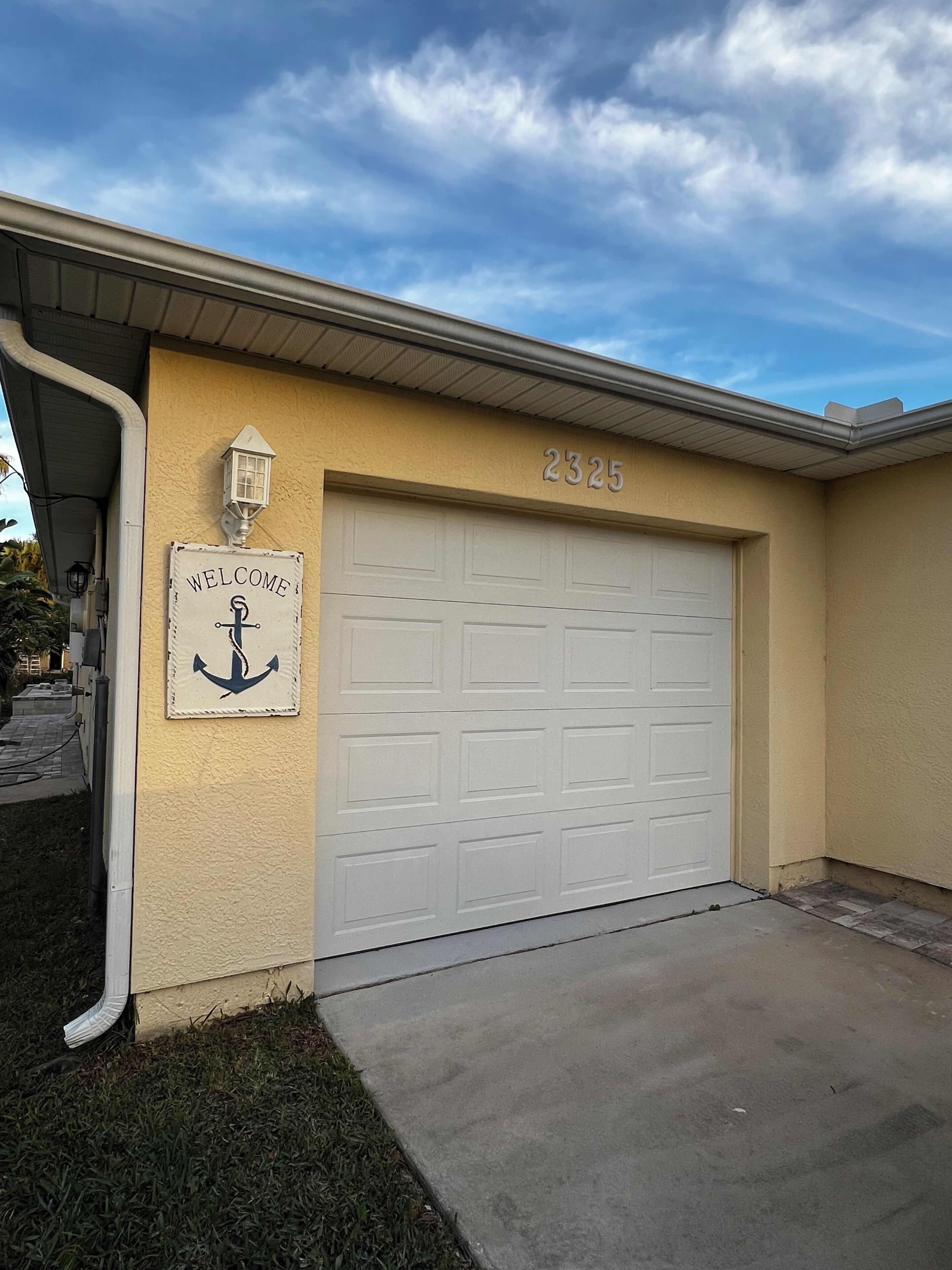 A residential garage with a 'Welcome' sign and a mailbox.