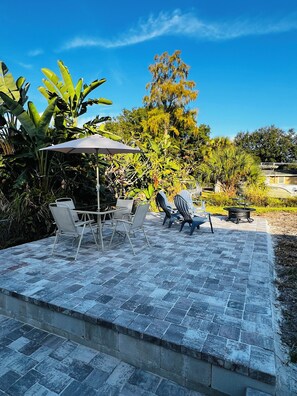 An outdoor patio with a stone floor, a table with chairs, a covered umbrella, and a fire pit. - West Melboburne Oasis, minutes to the beach! (Melbourne)