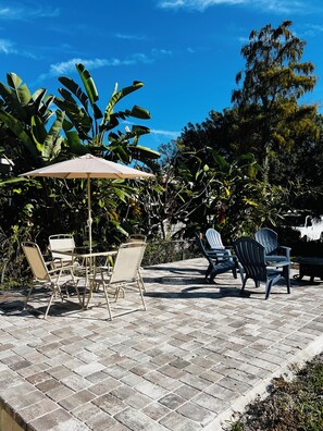 An outdoor patio with a table and chairs, surrounded by lush greenery and a clear blue sky. - West Melboburne Oasis, minutes to the beach! (Melbourne)