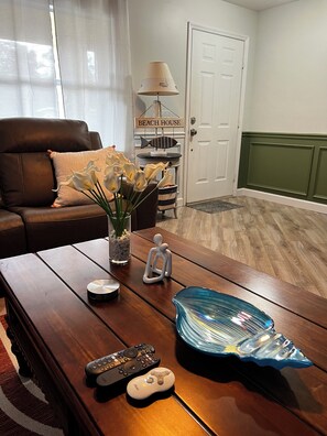 A living room with a brown leather sofa, a coffee table with remote controls, a decorative lamp, and a vase with flowers. - West Melboburne Oasis, minutes to the beach! (Melbourne)