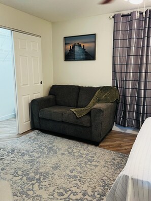 A room with a gray sofa, a patterned rug, a framed picture on the wall, and a plaid curtain. - West Melboburne Oasis, minutes to the beach! (Melbourne)