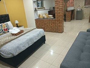 Una camera da letto moderna con un letto, un divano, una parete divisoria in mattoni e un piccolo tavolo con un bollitore.