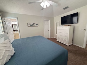 Ein Schlafzimmer mit Bett, Kommode, Fernseher und Deckenventilator.