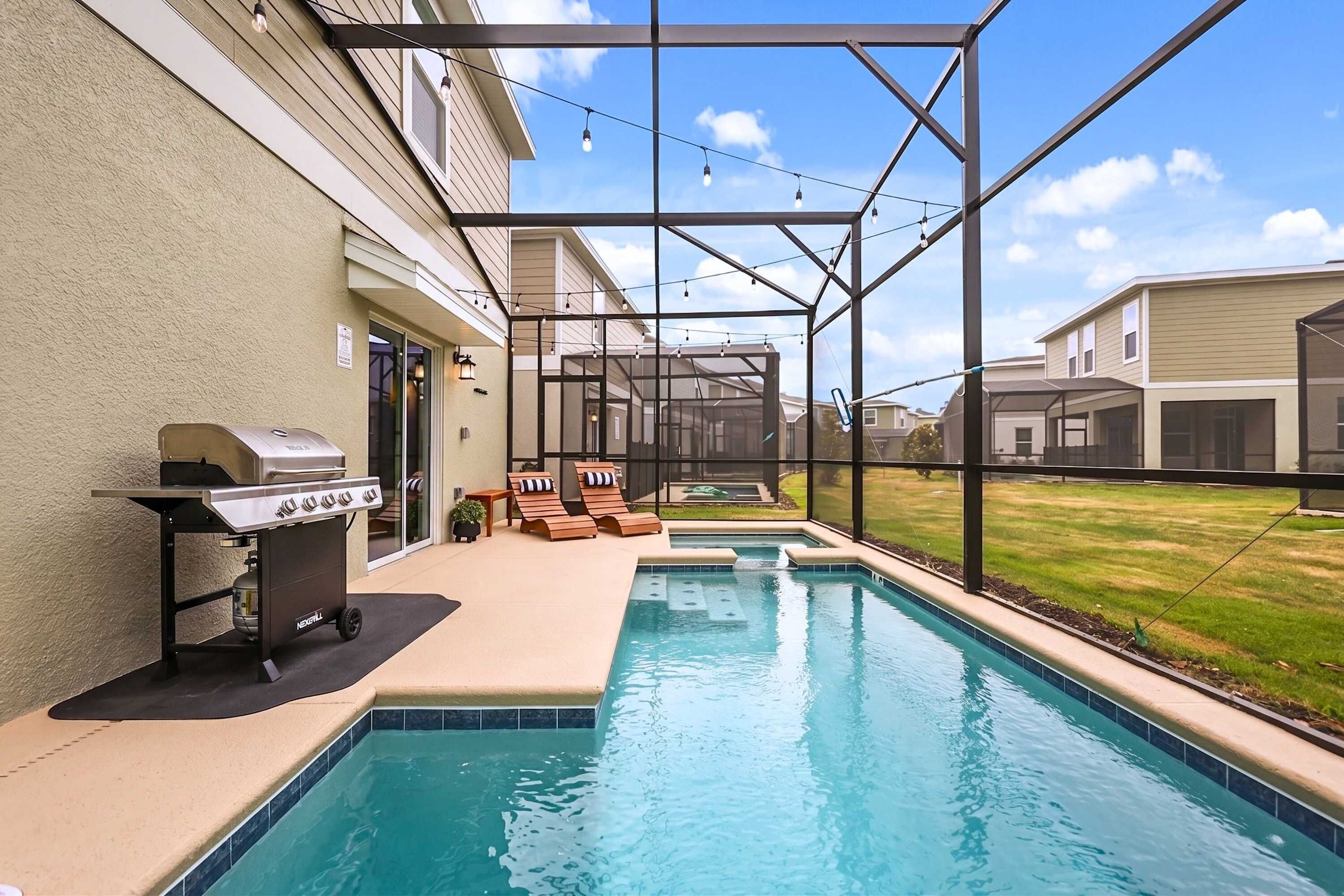 A swimming pool with a grill and lounge chairs, surrounded by a covered patio area.