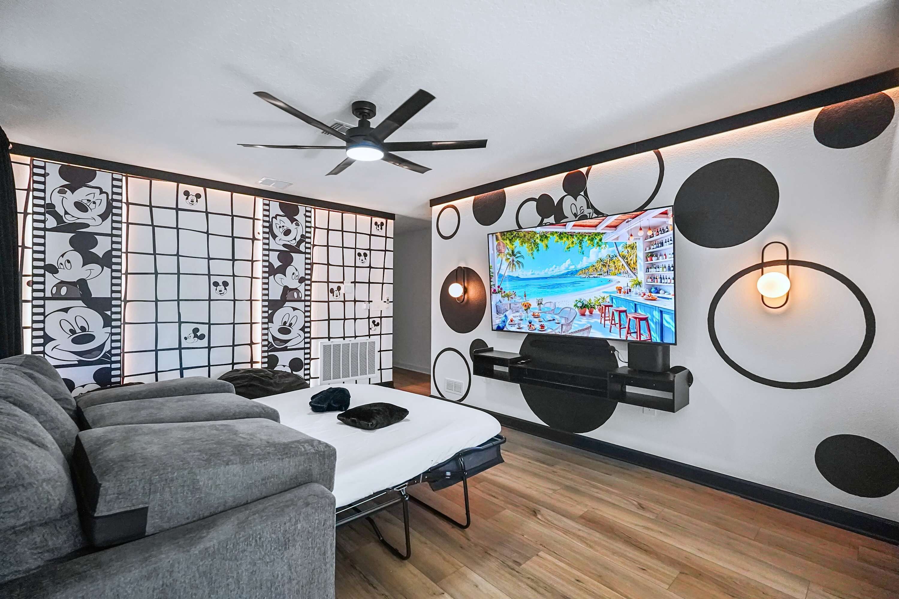 Una sala de estar moderna con un sofá, un televisor de pantalla plana montado en la pared, un ventilador de techo y paneles decorativos.
