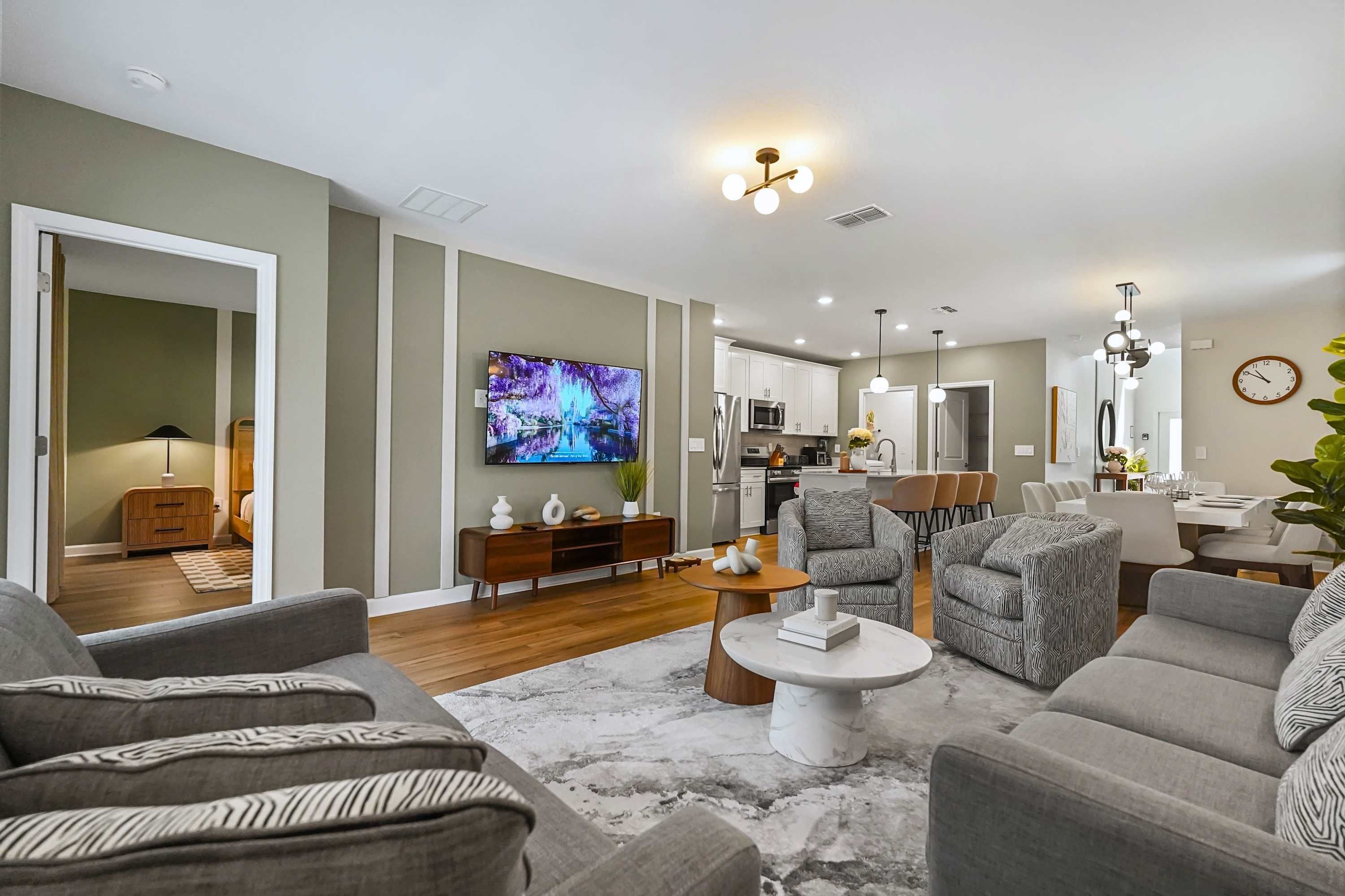 Una sala de estar moderna con un televisor de pantalla plana, sofás grises, una mesa de centro y una cocina al fondo.