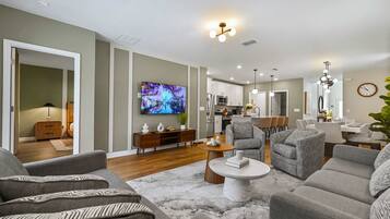 Una sala de estar moderna con un televisor de pantalla plana, sofás grises, una mesa de centro y una cocina al fondo.
