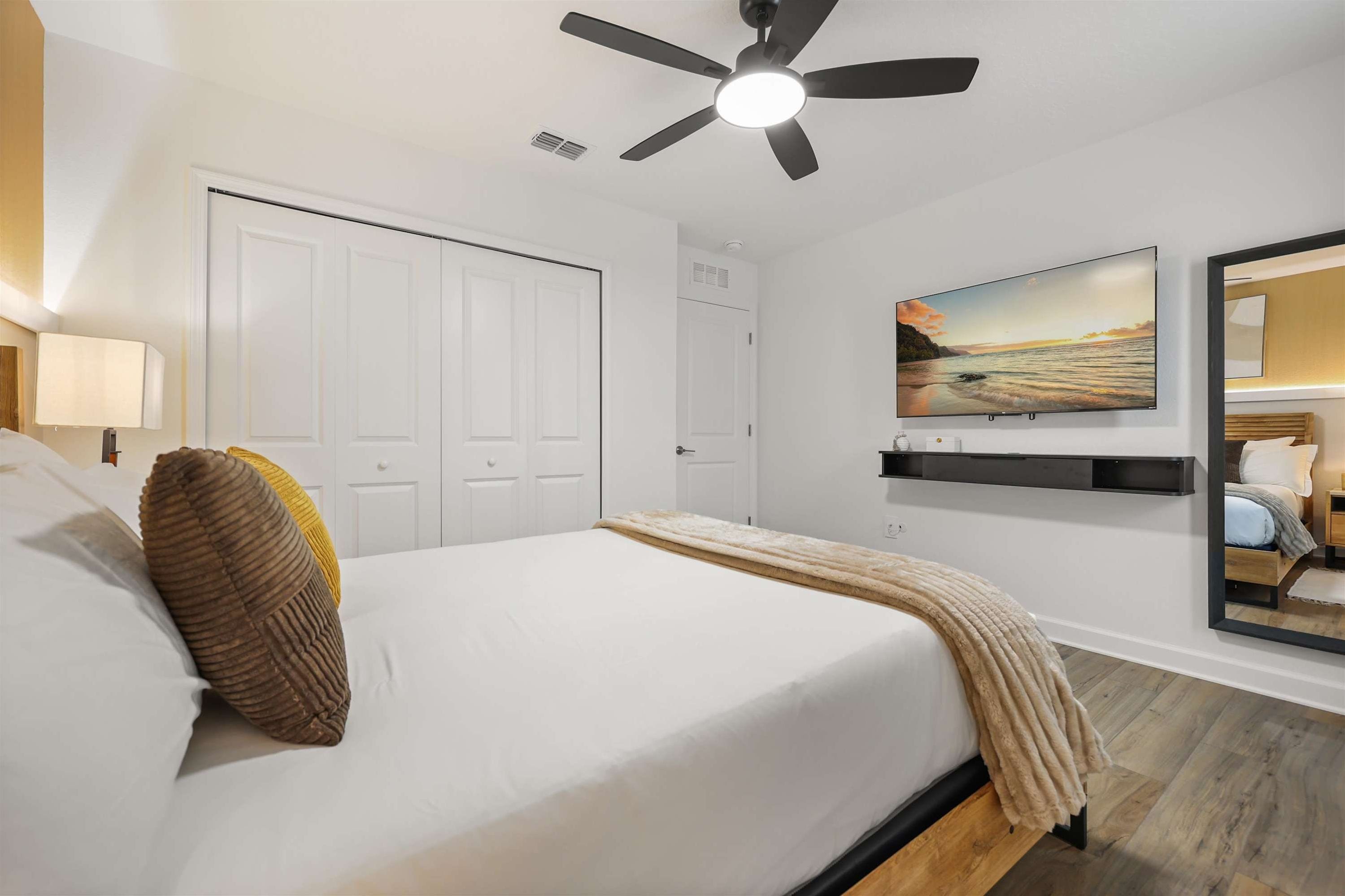 Ein Schlafzimmer mit einem Bett, einem Deckenventilator, einem an der Wand befestigten Fernseher und einem großen Spiegel.