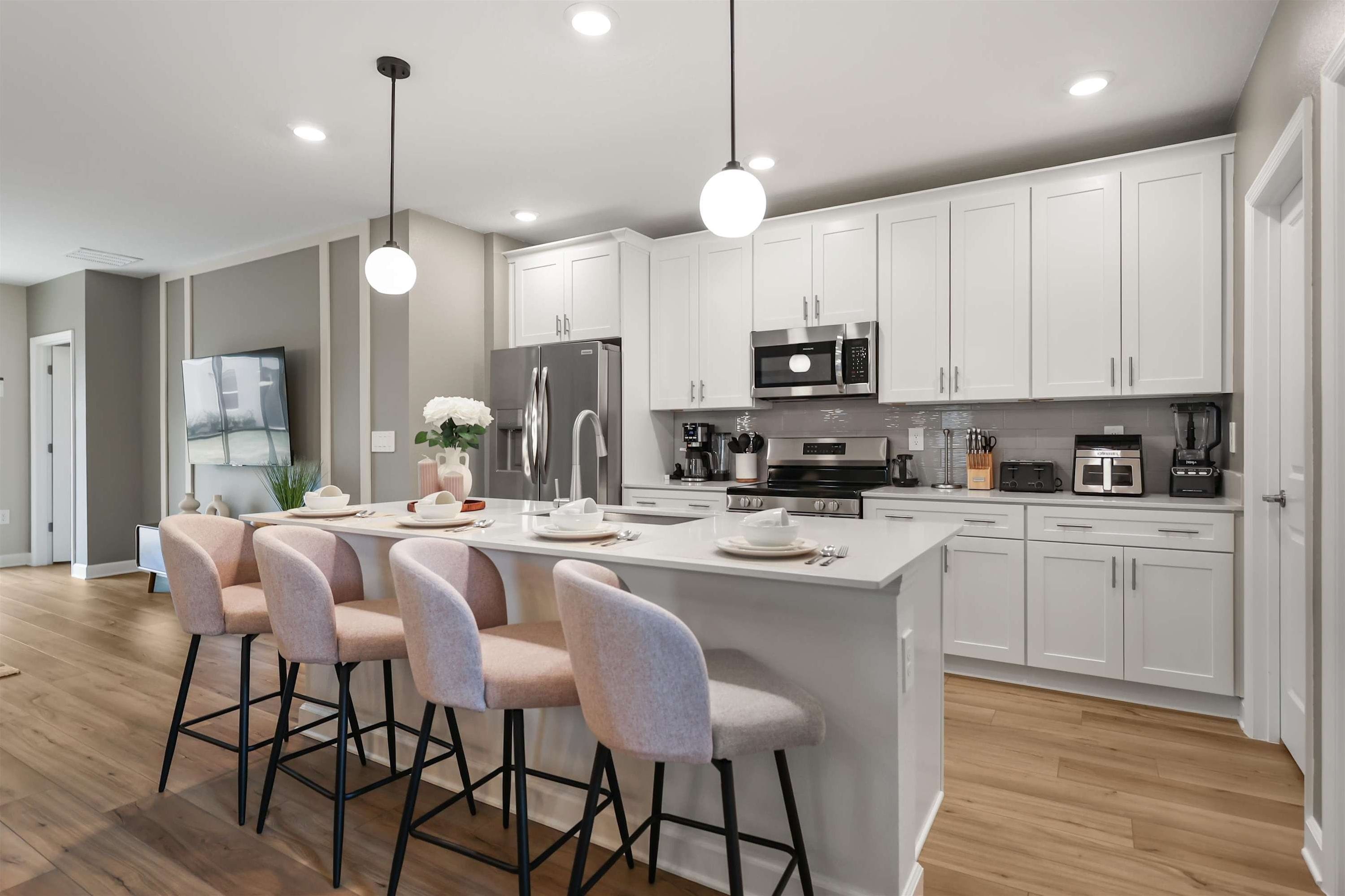 Una cocina moderna con armarios blancos, electrodomésticos de acero inoxidable y una isla central con taburetes de bar.