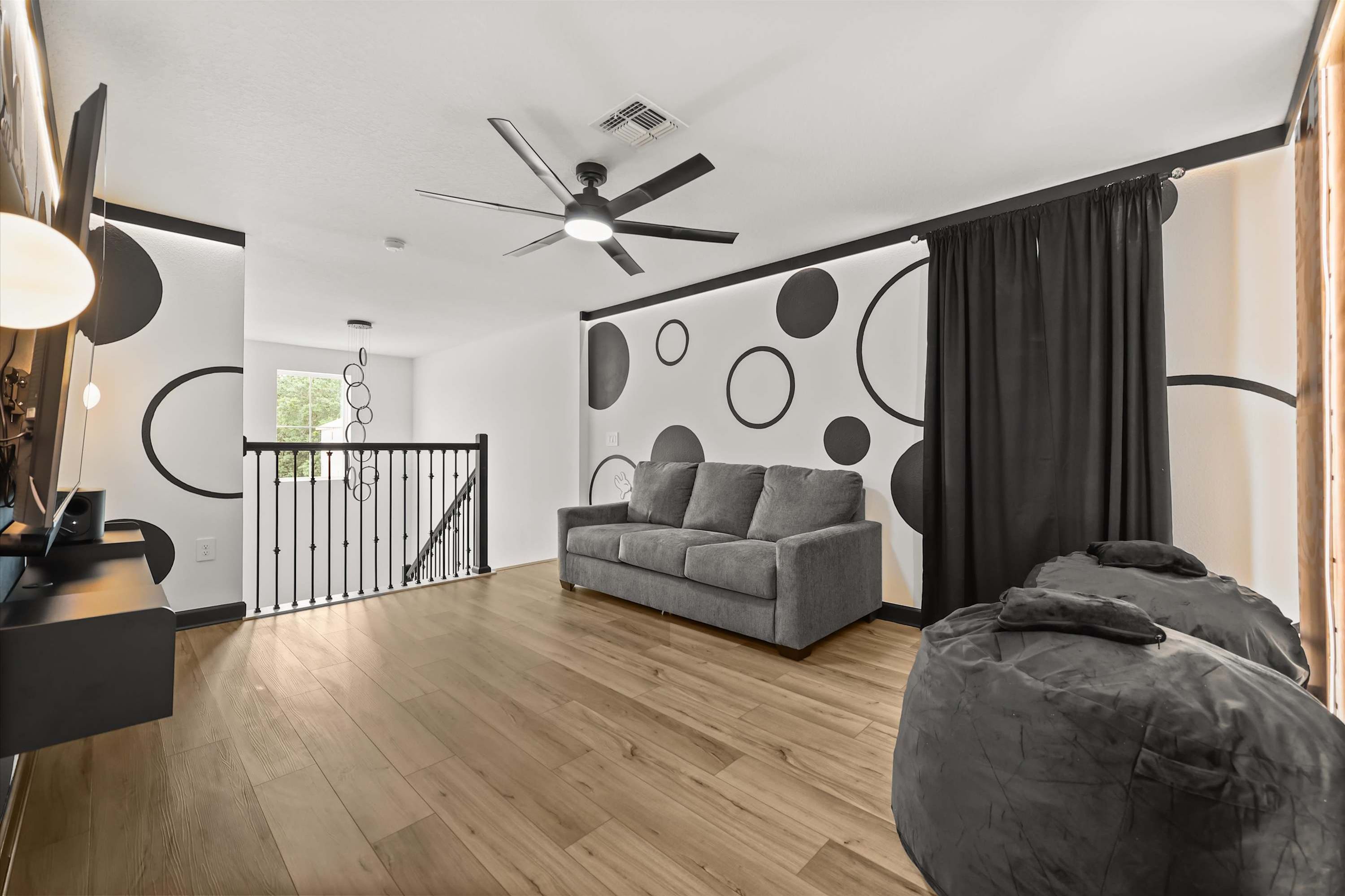 A modern living room with a grey sofa, a bean bag, a ceiling fan, and a staircase leading to an upper level.