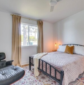 Ein Schlafzimmer mit einem Bett, einem Sessel, einem Fenster mit Vorhängen und einem Deckenventilator.