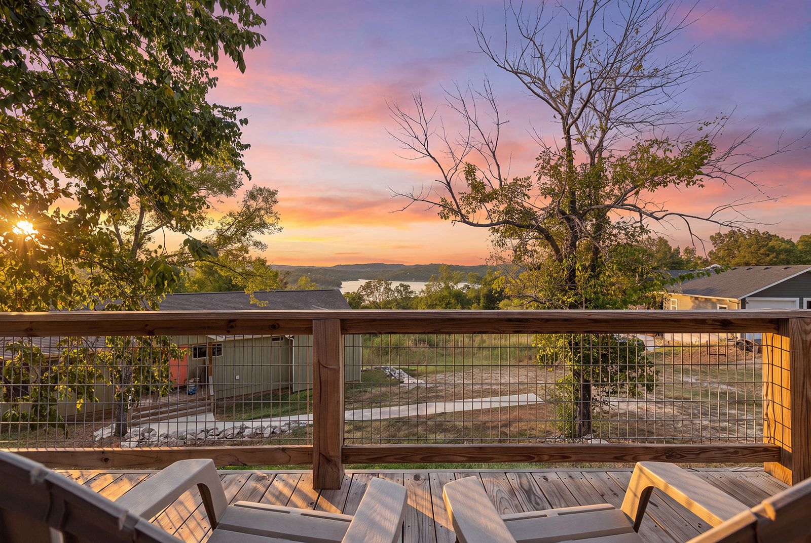 A wooden deck with metal railings, overlooking a fenced yard with a view of a lake and distant hills.