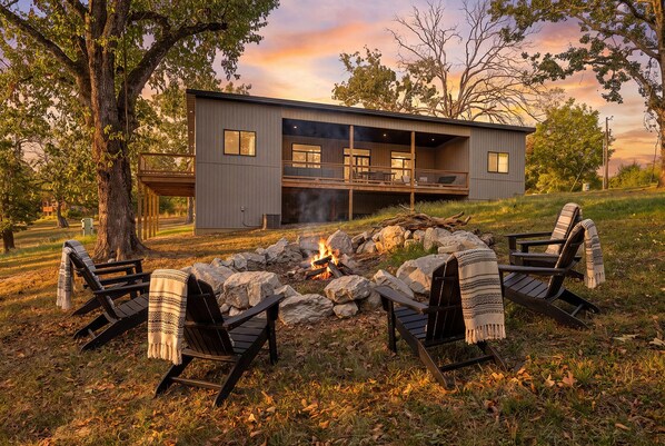 Een modern huis met een terras, een vuurkorf en vier Adirondack stoelen.