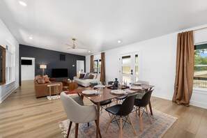 Een moderne woonkamer met een eethoek, een bank, een televisie en een plafondventilator.