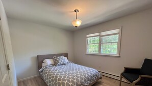A bedroom with a bed, a chair, a window, and a ceiling light.