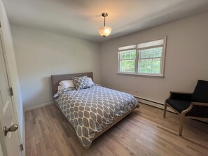 A bedroom with a bed, a chair, a window, and a ceiling light.