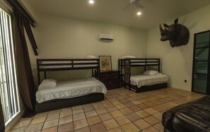 A room with two bunk beds, a ceiling fan, an air conditioning unit, a framed picture, and a large animal head decoration.