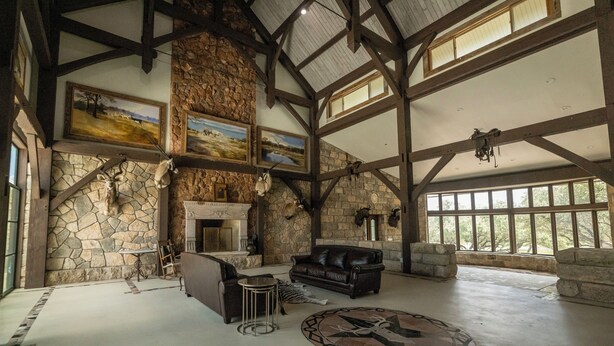 Una habitación amplia con chimenea de piedra, mobiliario de cuero y grandes ventanales.