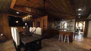 Un interior rústico con una mesa de comedor de madera, taburetes de bar y una zona de cocina.