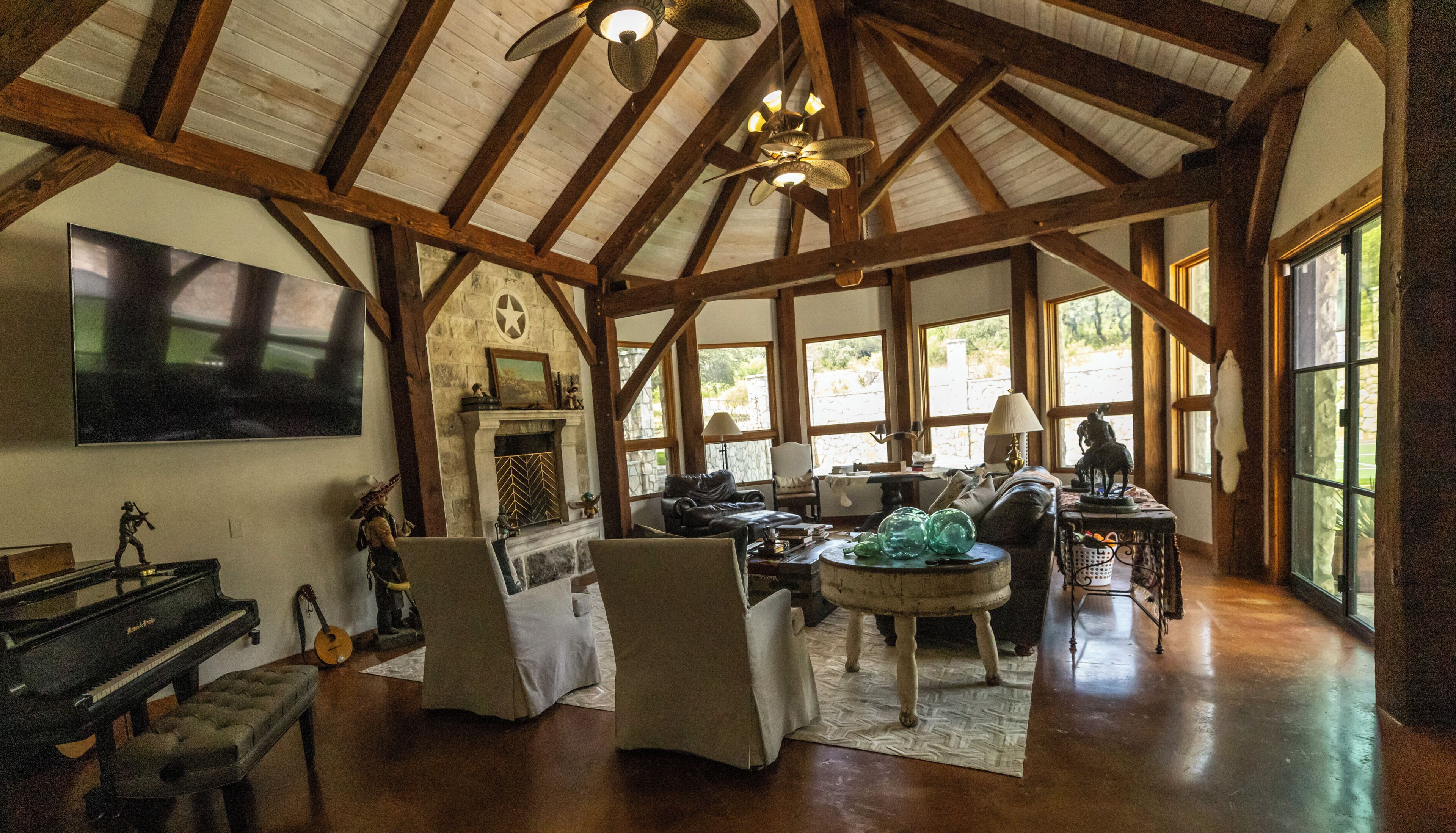 Una habitación amplia con techo alto, vigas de madera, chimenea, piano y un gran ventanal.