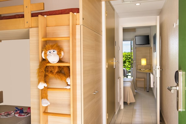 A room with a wooden ladder, a plush monkey toy, a bed, a TV, and a small table with a lamp.