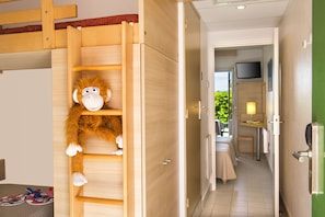 Una habitación con una escalera de madera, un peluche de mono, una cama, un televisor y una mesita con una lámpara.