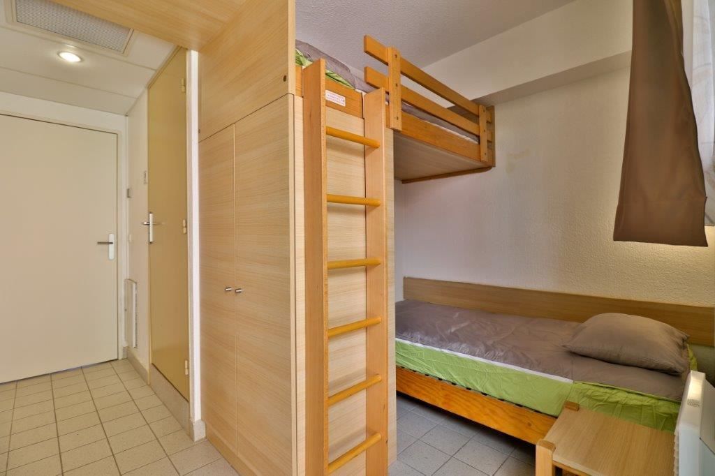 Une petite pièce comprenant un lit superposé, une armoire et une petite table.
