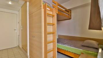 Une petite pièce comprenant un lit superposé, une armoire et une petite table.